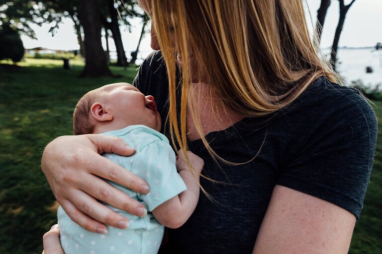 Mom holds newborn in the backyard while newborn smiles in her sleep.