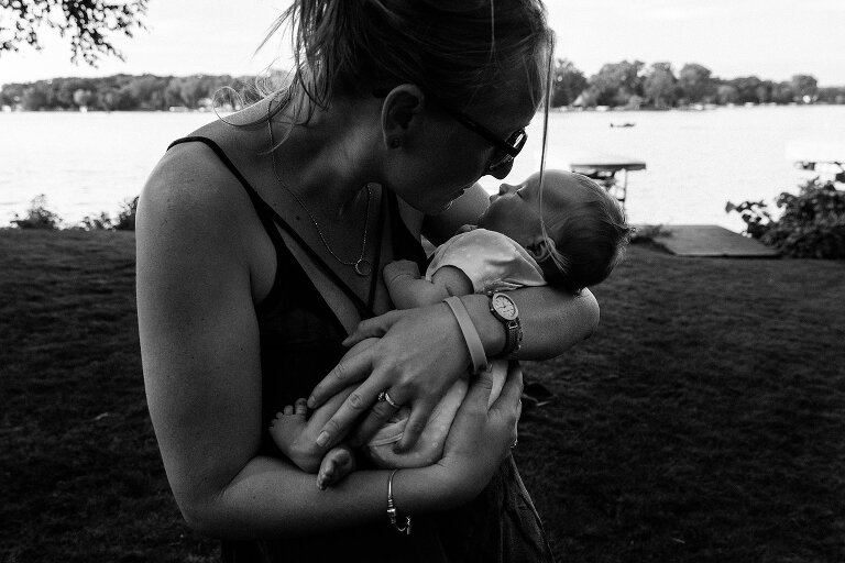 black and white. Aunt holds newborn with lake in the background