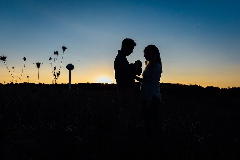 Silhouette of two parents holding their newborn against a sunset. 