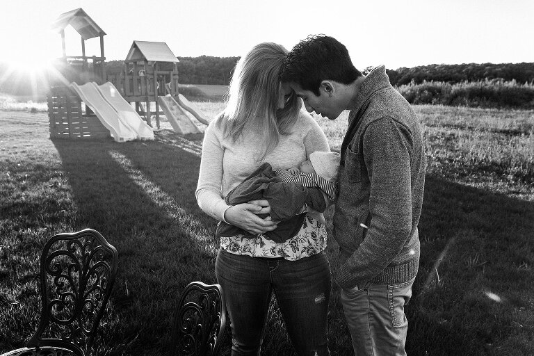 Black and white. New parents stand in the backyard and look at their newborn son while sun is shining. 