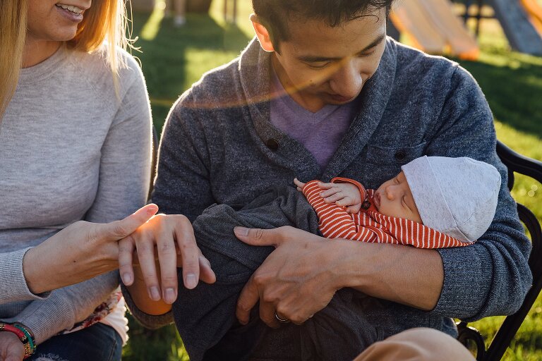Mom holds Dad's hand while Dad holds newborn in the backyard 