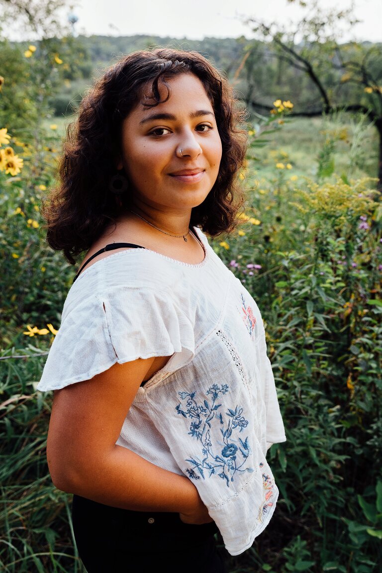 High school senior portrait, smiling and standing in a field of yellow flowers