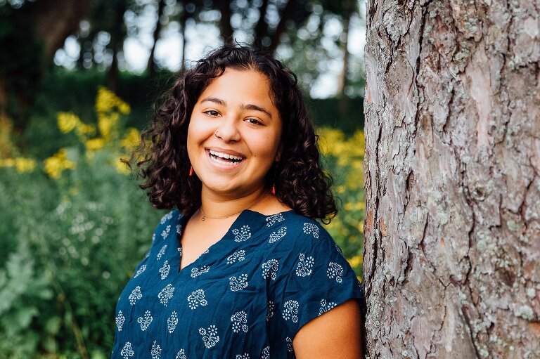 High school senior portrait, smiling and leaning against a tree