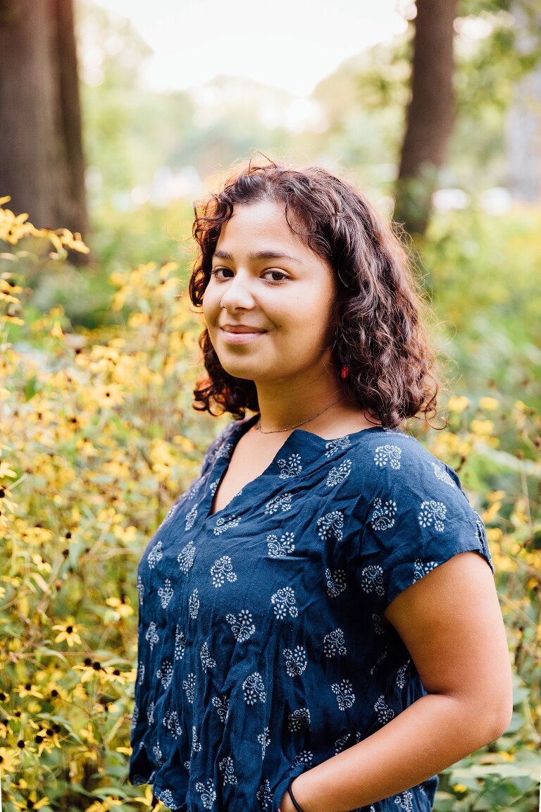 High school senior portrait, smiling and standing in a field of yellow flowers