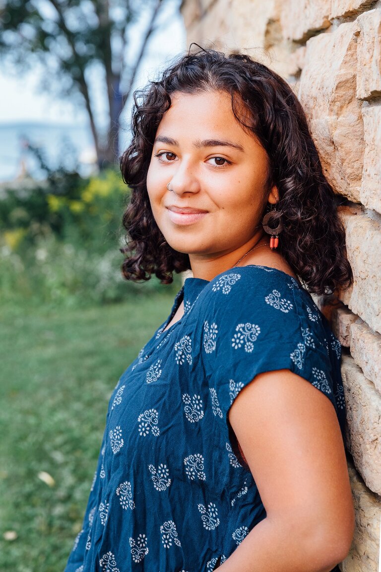 High school senior portrait, smiling and leaning against a wall with lake in the background