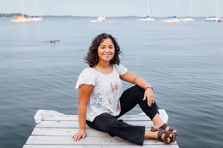 High school senior portrait, smiling and sitting on a pier at the lake