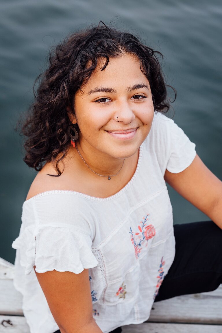 High school senior portrait, smiling and sitting on a pier at the lake