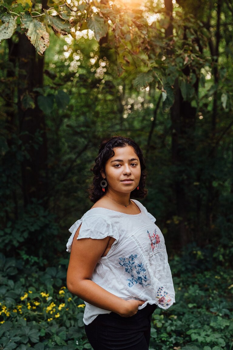High school senior portrait, standing in a forest with dappled light 