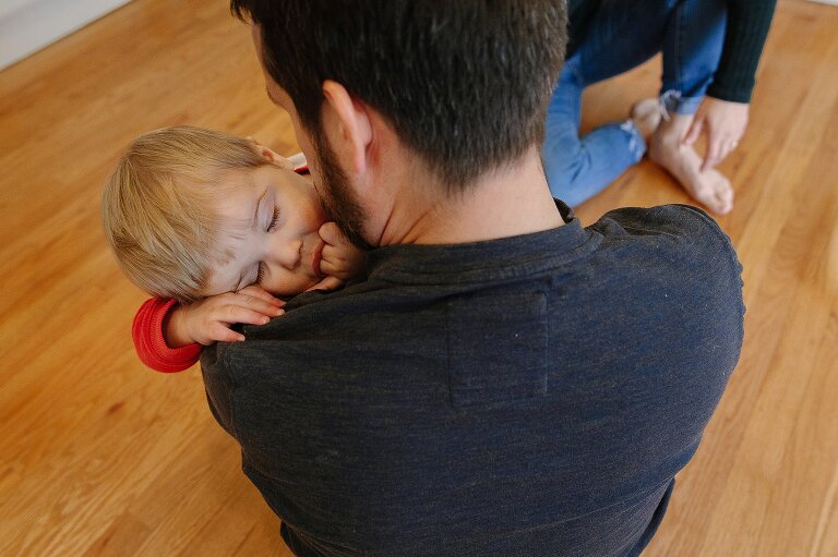 Boy snuggles into dad's shoulders, fall asleep with fingers in his mouth. 