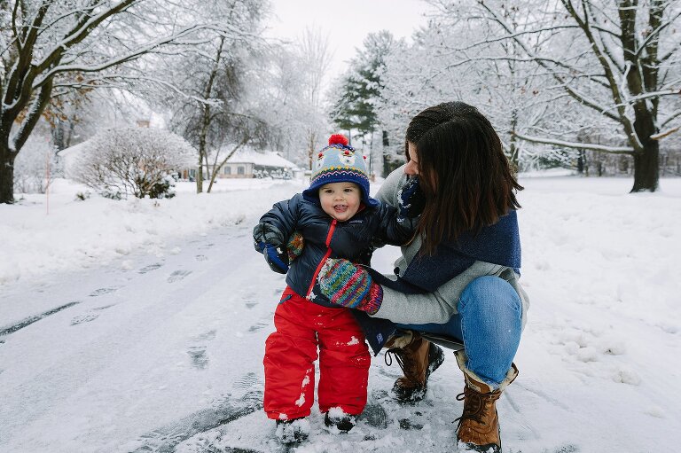Mom holds toddler on a snowy day. 