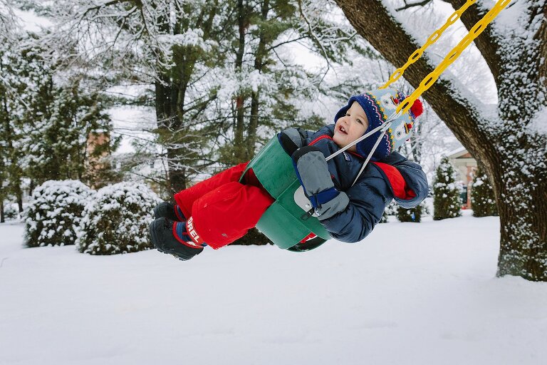 Colorful color weather clothes against snowy day with toddler on a swing