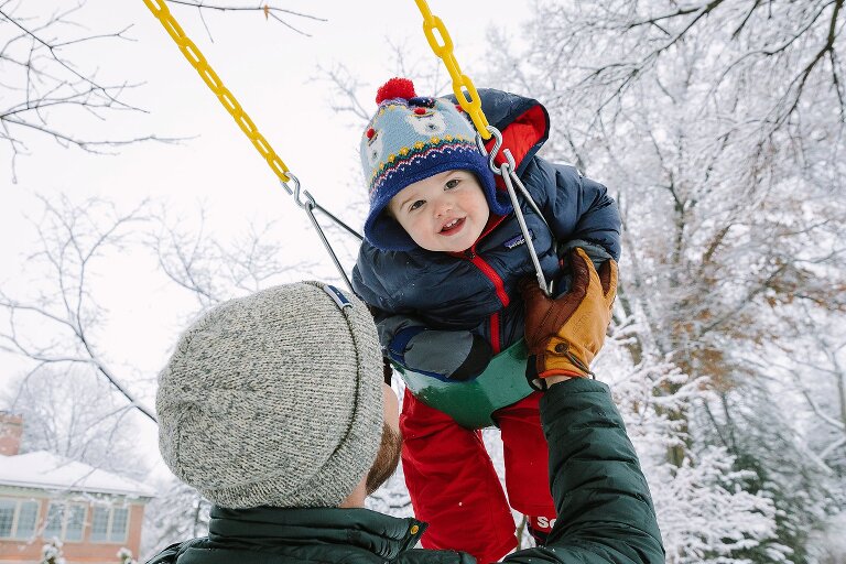 Dad pushes toddler in a swing on a snowy day