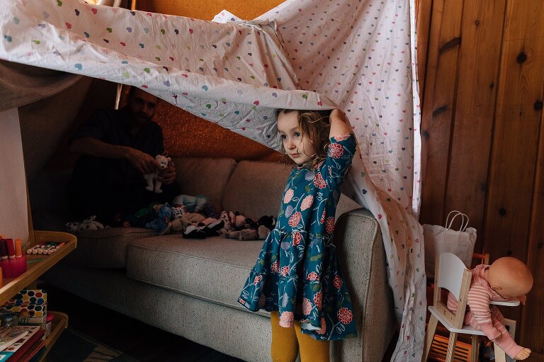 Girl plays in pillow fort with father. 