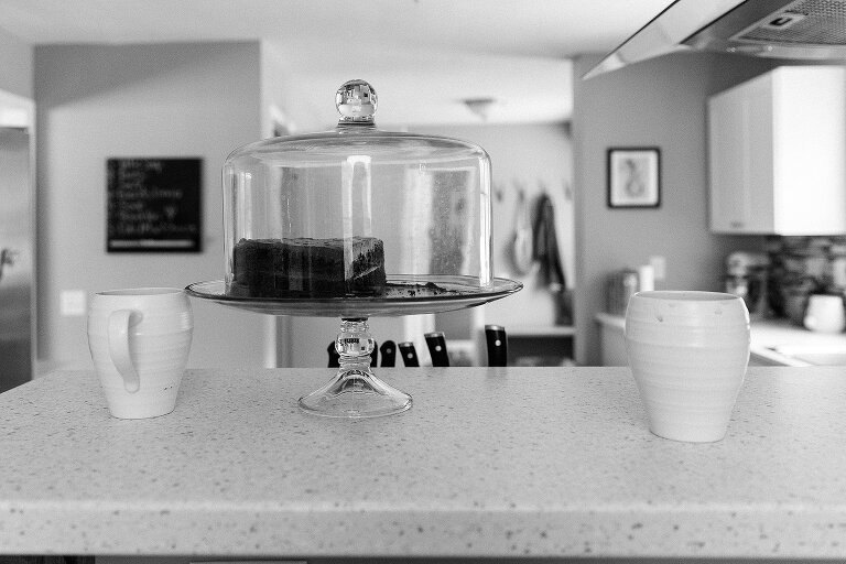 Black and white. Cake sits on cake stand next to white mugs. 