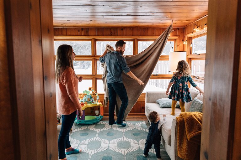 Father hangs up blanket while family stands behind him.