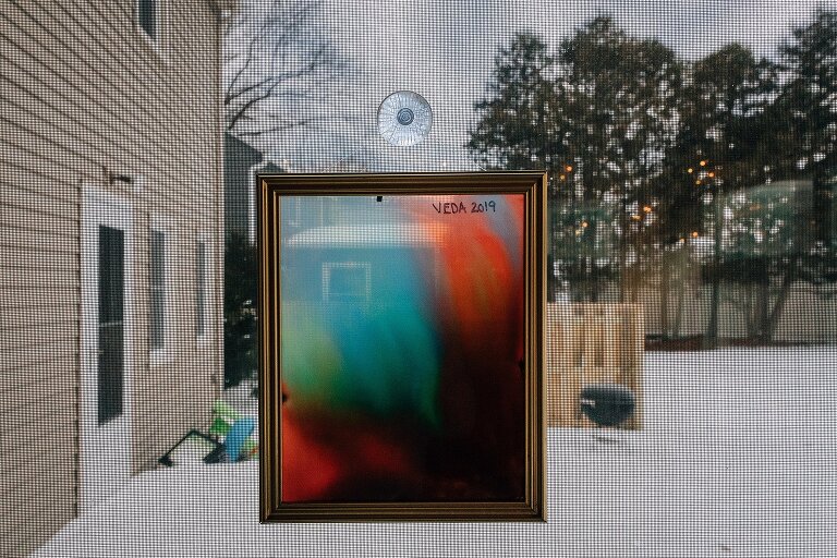 Art hangs in window with snowy backyard in view.