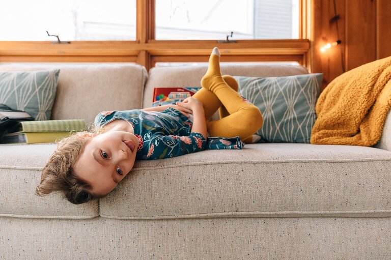 Girl lays upside down on sofa while sticking her tounge out. 