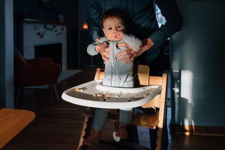 Father pulls infant out of messy highchair. 