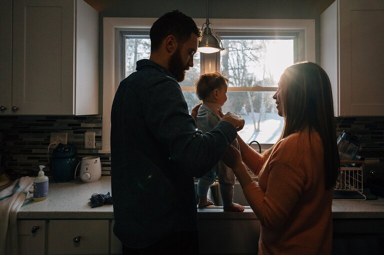 Mother and father hold infant while looking at the sunrise.