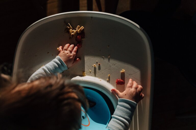 Light and shadow from top down view of dimpled infant hands eating on high chair tray