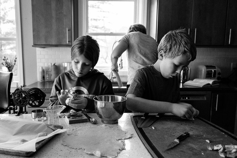 black and white of kids making extra mini pies while mom cleans rolling pin at the sink