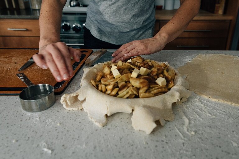 Open favorite apple pie filling, dotted with butter, as hands with motion blur press the sides
