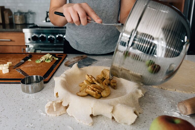 Mom pours favorite apple pie filling ingredients into prepared pie crust