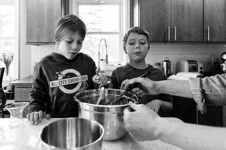 Hands hold bowl steady while girl pours lemon juice and boy watches on. 