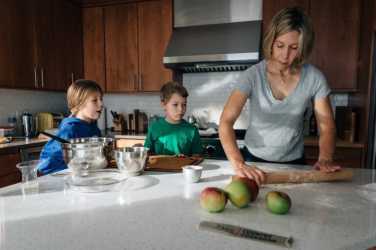 Kids watch mom roll out pie dough. Apples in foreground.