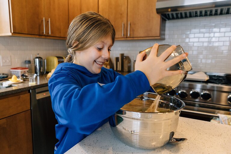 Girl smiles as she pours apple pie day ingredients into bowl of sliced apples