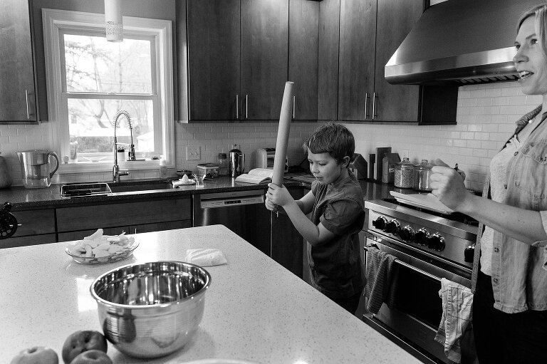 Boy smiles holding rolling pin ready to pound pie crust dough on counter
