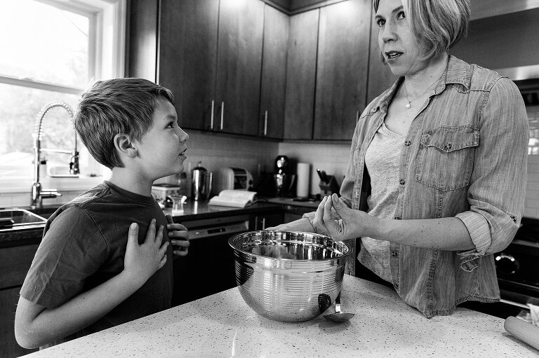 mom gestures with fingers to explain cooking technique while son presses hands to his chest and smiles