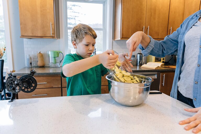Boy pours apples in bowl while mom points toward the bowl making Favorite Apple Pie