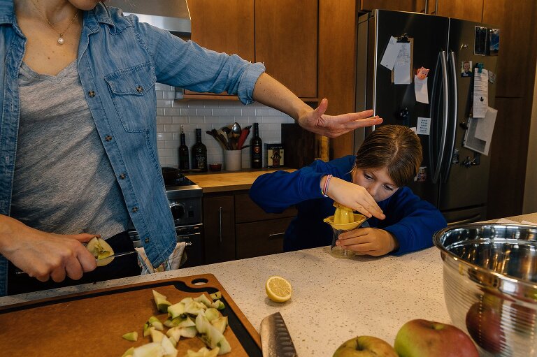 Mom slices apple in one hand and demonstrates to child how to press down on lemon juicer with other hand