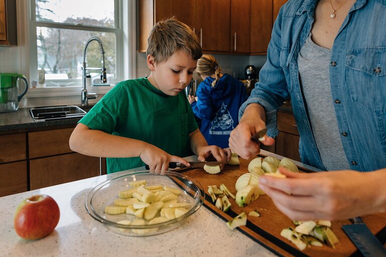Mom and boy peel and cut apples in foreground while girl gathers ingredients for favorite apple pie in the background making Favorite Apple Pie