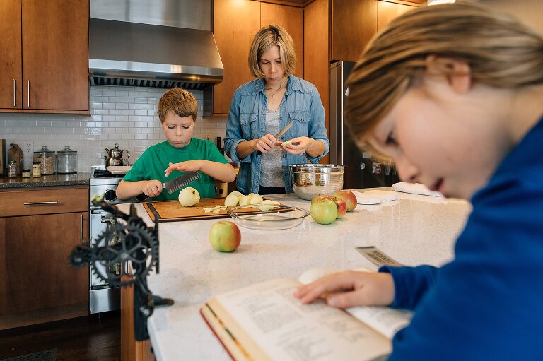 Girl studies recipe in foreground while mom and boy slice apples in the background