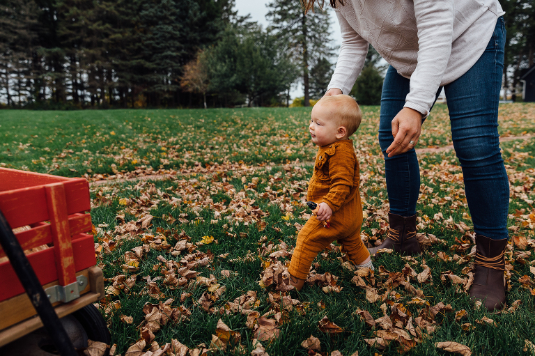 mom holds baby's hand to help her walk in the fall leaves