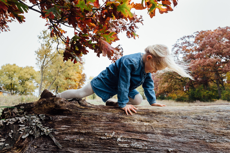 girl climbing on a fallen log with oak leaves above here and wind sweeping her hair