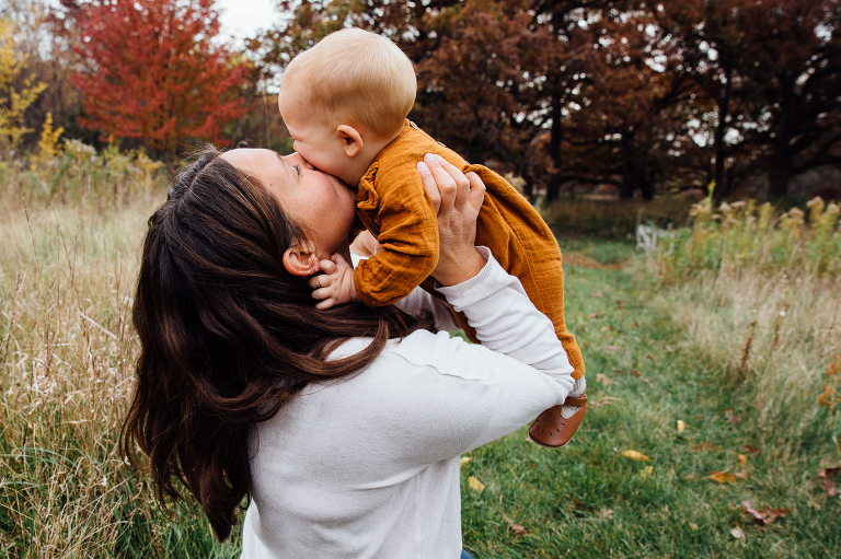 mom lifts baby for a kiss while on a fall trail 