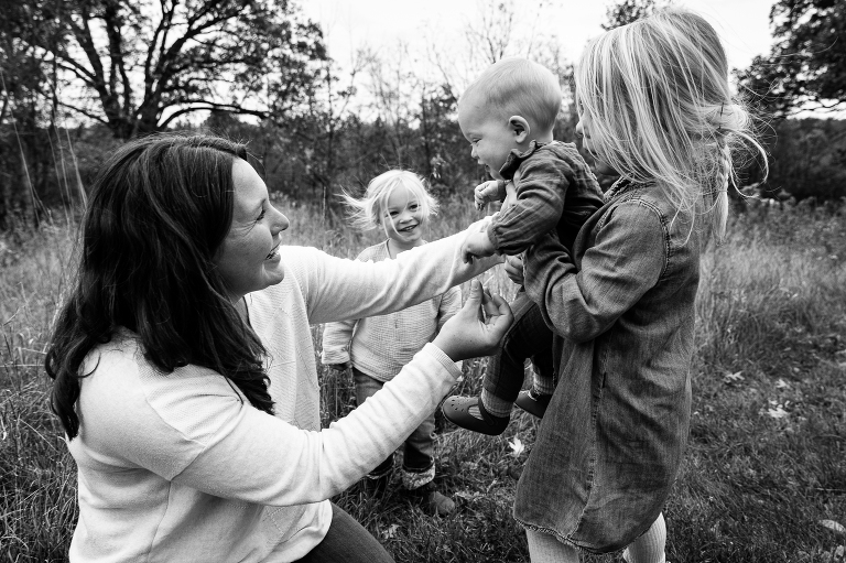 mom and her three girls smile and reach for each other; black and white 