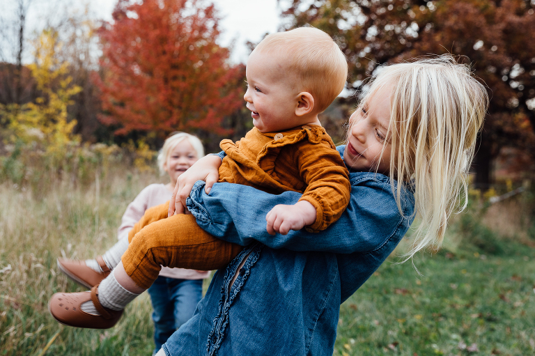 Older girl lifts baby while middle girl smiles in the background