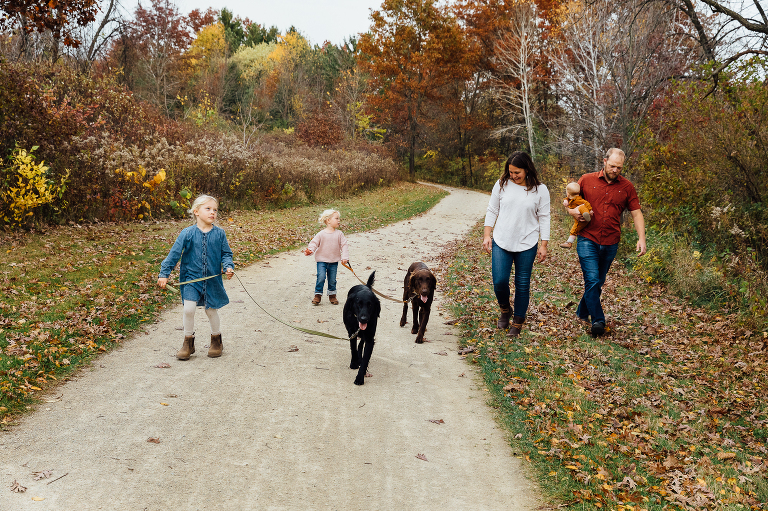 Family of 5 with three young girls and two dogs walk on an autumn forest path