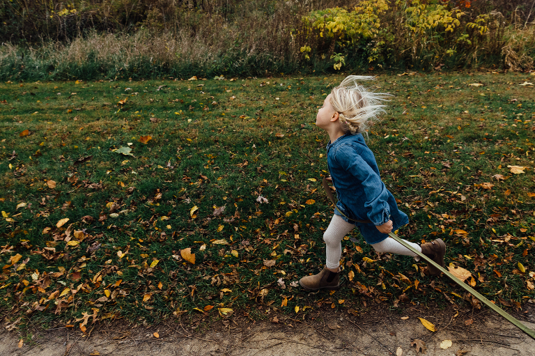 girl runs in the grass while holding dog leash, wind in her hair
