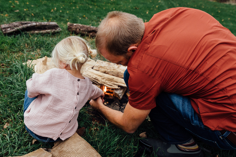 dad helps young daughter safely light a backyard fire for s'mores