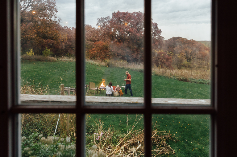 view through window panes of family preparing a backyard fire on an autumn day