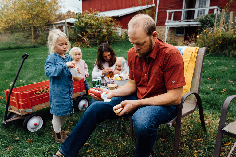 dad holds ketchup in one hand and hot dog in a bun in the other as mom and three girls circle around him