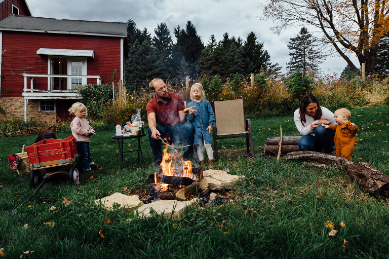 family of five semi-circle around a fire pit while roasting marshmallows for s'mores