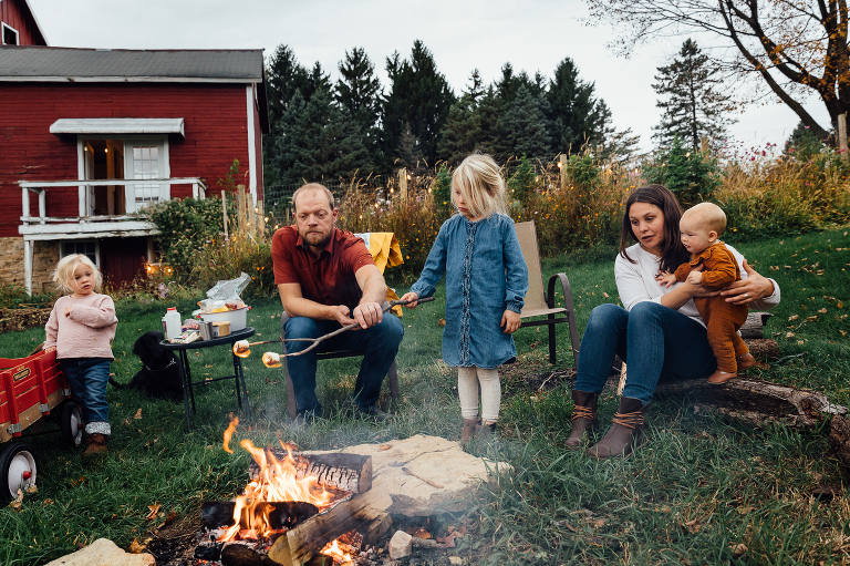 family of five semi-circle around a fire pit while roasting marshmallows for s'mores