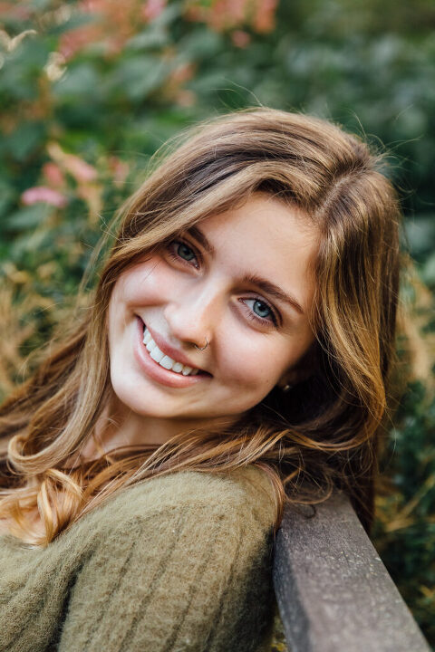 smiling senior girl in an olive colored sweater in nature 