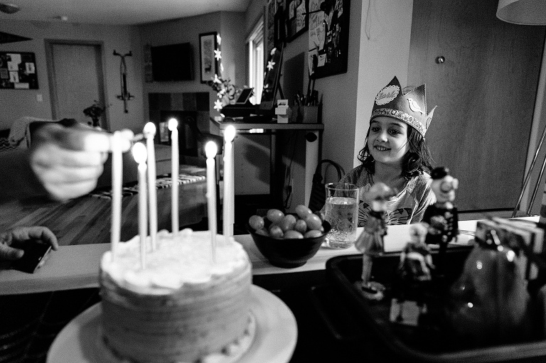 Girl wears birthday crown as a hand lights candle on a birthday cake